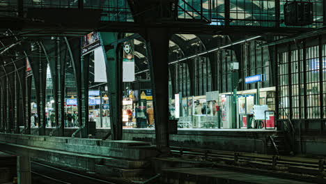 Dentro-De-La-Estación-De-Metro-De-Berlín-Friedrichstrasse-Con-Viajeros-Y-Trenes-Acelerando-La-Vida-Nocturna-Iluminada-Lapso-De-Tiempo