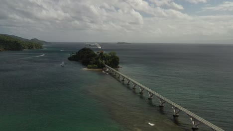 Ascending-aerial-shot-of-Pedestrian-Bridge-at-Samana-Bay-with-luxury-Cruise-Ship-leaving-Harbor-during-sunny-day,Dominican-Republic