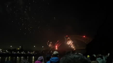 Crowd-watch-colourful-fireworks-exploding-on-Silver-Jubilee-bridge,-Widnes-at-night