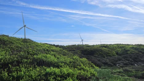 Three-wind-turbines-moving-with-sand-dunes-in-foreground,-one-turbine-broken-down