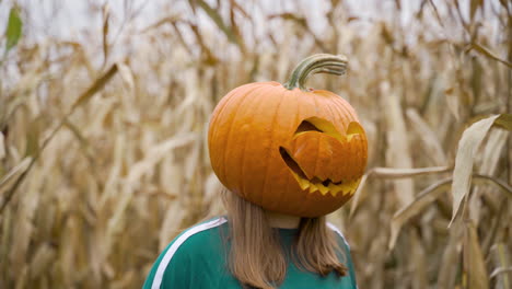 Woman-With-Carved-Pumpkin-On-Her-Head-Looking-Around-At-Corn-Field-During-Daytime