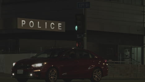 Establishing-the-local-police-station-building-entrance-signage-at-night-with-some-traffic-movement-in-the-foreground,-tilt-down-reveal-shot