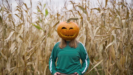 Geschnitzter-Halloween-Kürbis-Auf-Dem-Kopf-Eines-Blonden-Mädchens-Im-Mais-Ackerland
