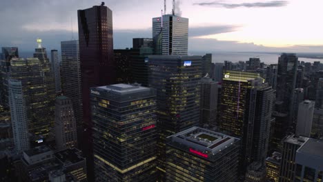 Aerial-view-around-illuminated-skyscrapers-in-downtown-Toronto,-dusk-in-Canada---circling,-tilt,-drone-shot