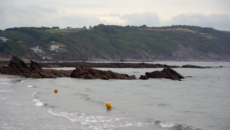 Yellow-warning-buoys-bob-up-and-down-in-the-surf-of-East-Looe-beach-in-Looe,-Cornwall,-England,-UK