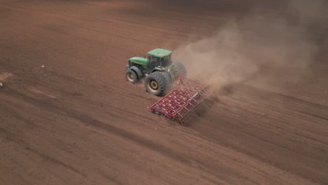 Dusty-work-as-farm-tractor-pulls-tine-harrow-in-field-before-planting