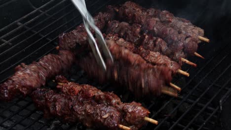 Moving-juicy-kebabs-around-the-grill-with-tongs-on-a-barbecue,-close-up