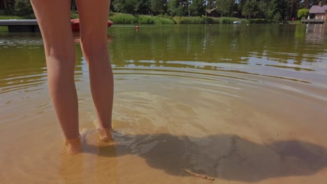 Young-girl-bare-foot-in-shallow-water-on-side-on-lake-in-Summer