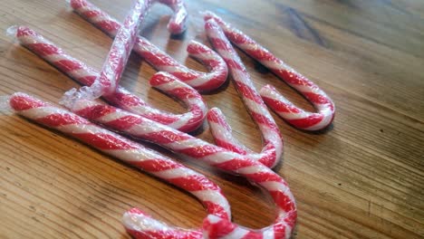 Shiny-plastic-wrapped-striped-Christmas-candy-canes-on-wooden-kitchen-table-home-decoration-rotating-left