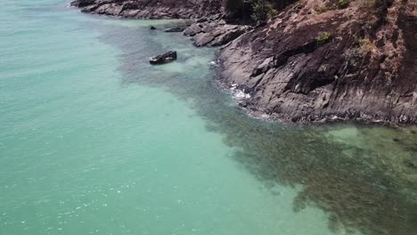 Drone-aerial-slowly-moving-and-panning-up-over-tropical-blue-water-and-beach-cliff-side