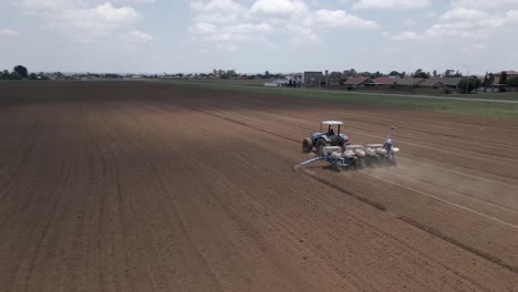 Orbiting-aerial-of-tractor-pulling-seed-planter,-seeding-on-crop-farm
