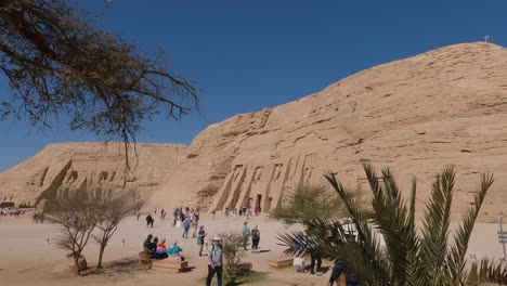Tourists-in-front-of-the-temple-entrance,-statues-of-Ramses-II,-temple-carved-out-of-the-mountainside-in-Abu-Simbel