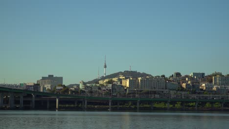 Seoul-Namsan-Tower-and-Yongsang-Villas-from-the-riverbank-of-Hangang-river,-Traffic-from-Hannam-bridge-to-Gangbyeon-Expressway-road-on-sunset-cloudless-blue-sky