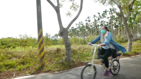 Grupo-De-4-Mujeres-Montando-Bicicletas-En-Caminos-Rurales-Durante-El-Día-Soleado-Y-Pasando-Por-Delante-De-La-Cámara,-Filmada-Como-Una-Toma-De-Gran-Angular-Desde-El-Lado-Izquierdo-De-Los-Ciclistas