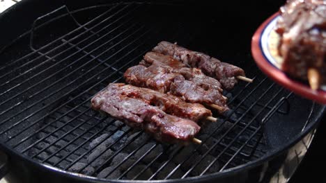 Placing-shish-kebabs-onto-a-grill-during-a-barbecue,-close-up
