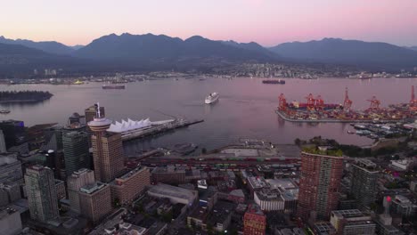 Aerial-view-over-the-city-centre,-towards-a-cruise-liner-on-the-Vancouver-Harbour-sea,-dusk-in-BC,-Canada
