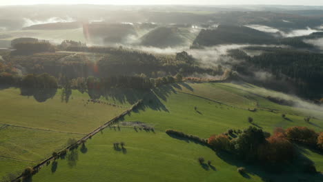 Foggy-Countryside-Landscape-With-Green-Fields-And-Forests-In-Sommerain,-Belgium---aerial-pullback