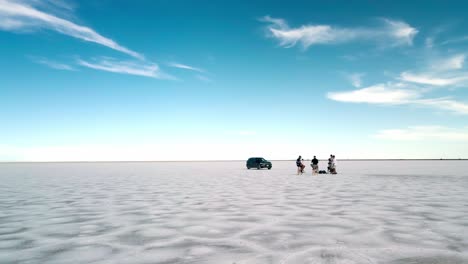cinematic-orbiting-around-a-crew-filming-an-interview-in-a-remote-area-bonnesville-salt-flats,-utah,-usa,-black-car,-blue-skyes-and-clouds