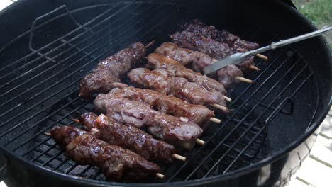 Turning-marinated-beef-and-pork-kebabs-on-a-grill-using-tongs-over-an-open-fire