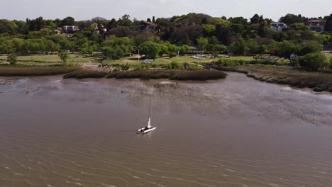 Aerial-circling-around-man-dragging-catamaran-out-of-water,-Vicente-Lopez-coast-in-Buenos-Aires