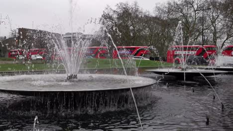 Busy-UK-street-with-double-decker-buses-and-cars-behind-water-fountain