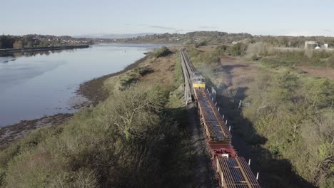 Following-aerial-of-freight-train-hauling-railroad-tracks-along-river