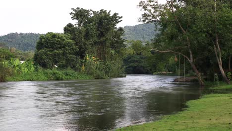 4k-Schöne-Weitwinkelaufnahme-Eines-Flusses-Mit-Seilschaukel,-Die-An-Einem-Baum-In-Thailand-Hängt
