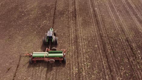 Aerial-follow-shot-of-agricultural-tractor-plowing-field-with-machinery-during-sunny-day---Tracking-shot