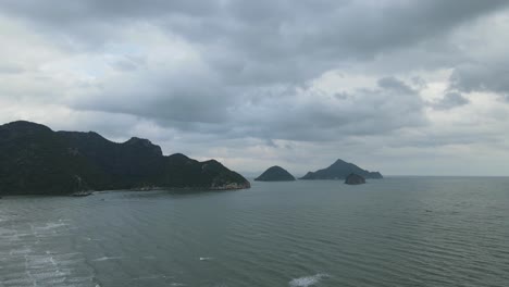 Ascending-aerial-footage-revealing-the-waves-down-below-the-mountains-and-Islands-then-the-lovely-sky-with-gray-clouds,-Sam-Roi-Yot-National-Park,-Prachuap-Khiri-Khan,-Thailand