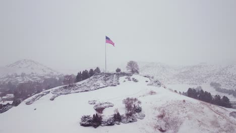 Drone-shot-of-an-American-flag-waving-on-top-of-a-snow-covered-hill