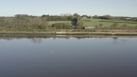Low-flight-over-glassy-river-to-freight-train-passing-green-farmland