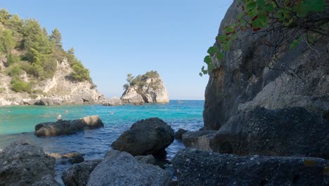 Tourists-bathing-on-turquoise-water-of-Golfo-beach,-picturesque-beach-surrounded-by-Rocks,-Parga