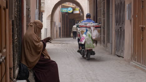 Marrakesch-Frau-Mit-Burka,-Die-Mit-Dem-Handy-Telefoniert,-Während-Motorradfahrer-Durch-Die-Schmale-Gasse-Von-Marrakesch-Gehen