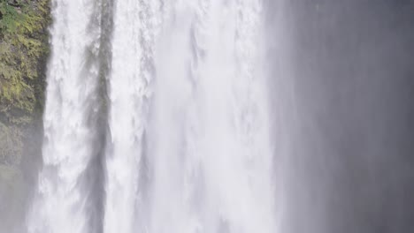 Tourist-standing-in-front-of-powerful-Skogafoss-waterfall-in-Iceland