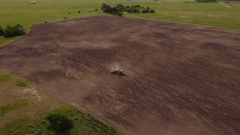 Aerial-orbit-shot-of-driving-tractor-plowing-farmland-during-sunny-day---Dust-rising-up---Rural-Province-of-Buenos-Aires,Argentina---4K-Drone-footage