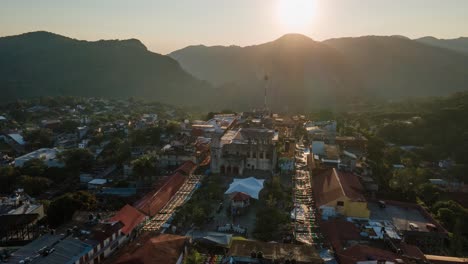 Orbiting-hyperlapse-aerial-view-of-the-square-in-town-Xilitla,-sunrise-behind-mountains-in-the-background