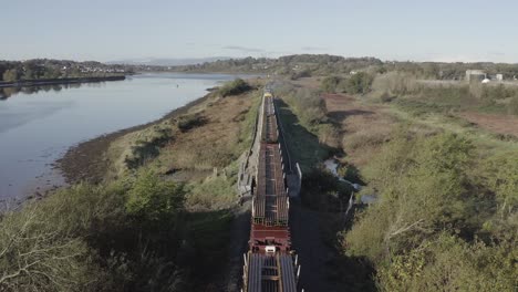 Tonnes-of-railroad-track-hauled-by-train-beside-River-Suir,-Ireland