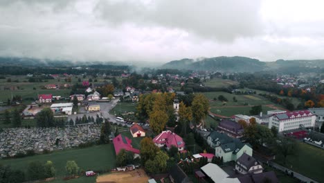 Aerial-Footage-of-Foggy-Countryside-Landscape,-Clouds,-Households-and-White-Church-in-Autumn-Day