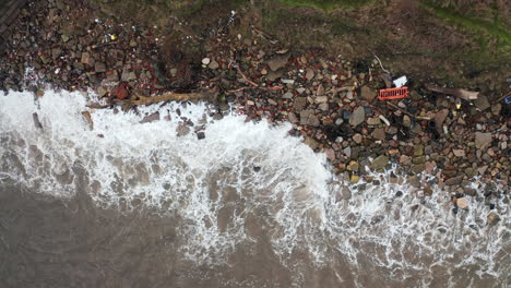 Eine-Luftbildkamera-Schwenkt-Entlang-Eines-Mit-Müll-übersäten-Strandes,-Während-Wellen-über-Das-Ufer-Schlagen