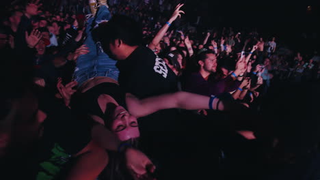 Spectators-Crowd-in-Front-of-Stage-Cheering-Carrying-Young-Lady-on-Arms-at-Rock-Music-Concert-Show,-Security-Agents-Supervising,-Inside-Arena-With-Colorful-Flashing-Spotlights