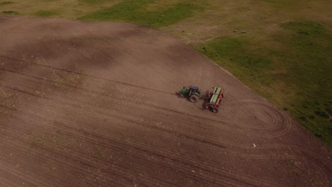 Aerial-shot-of-tractor-plowing-farm-field-with-brown-soil-in-agricultural-area-of-Argentina---Wild-birds-flying-over-field-and-pecking-seed