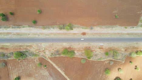 Top-down-aerial-of-a-single-white-car-driving-over-road-in-rural-Kenya