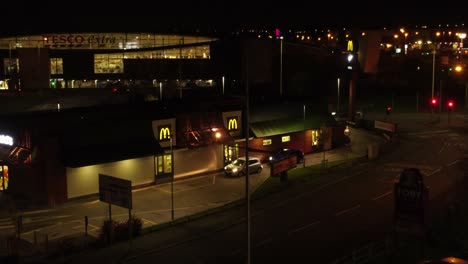 Vehicles-waiting-outside-McDonalds-fast-food-drive-through-illuminated-at-night-in-Northern-UK-town-aerial-orbiting-view-rising-right