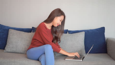 Asiatische-Lächelnde-Junge-Frau,-Die-Auf-Couch-Sitzt-Und-Laptop-notizbuch-Verwendet,-Das-Bildschirmschreibnachricht-Betrachtet,-Dame,-Die-Auf-Computer-browsing-surfen-internet-social-media-studiert-Oder-Online-Zu-Hause-Arbeitet