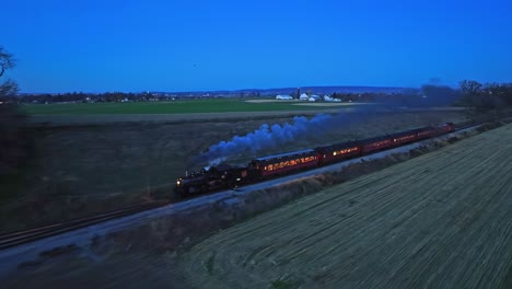 A-Drone-Night-View-of-a-Steam-Passenger-Train-Approaching-on-a-Single-Track-Traveling-Thru-Farmlands-Seeing-the-Lights-in-the-Coaches