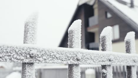 Frozen-fence-covered-with-snow-and-ice,-cold-winter-day,-blurred-house-behind