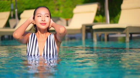 Damenhafte-Asiatische-Frau-Drückt-Wasser-Aus-Den-Haaren,-Während-Sie-In-Einem-Schwimmbad-Badet-Und-Ihr-Nasses-Haar-Berührt,-Gesicht-Nahaufnahme,-Thailand