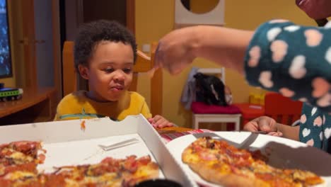 Adorable-and-very-espressive-two-year-old-black-baby-eats-pizza-at-home-fed-by-mum-with-a-fork