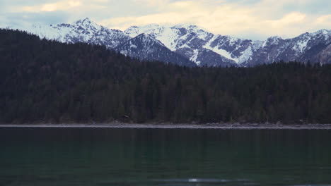 Peaceful-lake-Eibsee-rippling-water-and-woodland-forest-shoreline-under-majestic-snowy-glacier-mountain-range