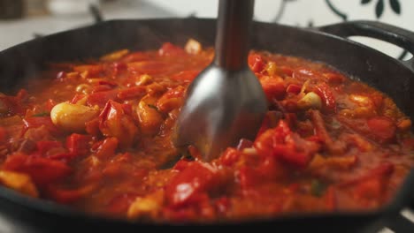 Mashing-vegetable-mix-with-blender-inside-frying-pan-during-cooking